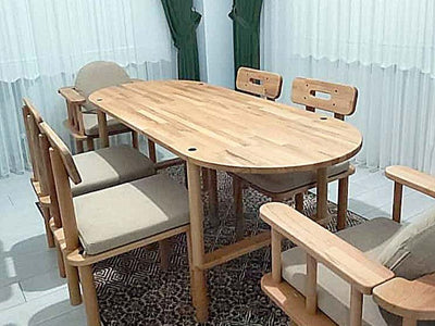 Tül perde önünde oval ahşap yemek masası; çevresinde krem minderli ahşap kollu sandalyeler