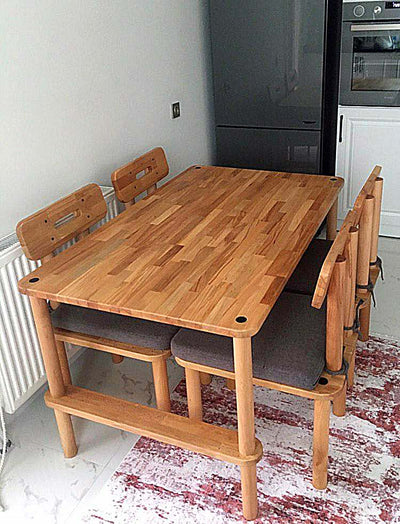 Mutfakta ahşap yemek masası; çevresinde ahşap sandalyeler ve gri minderli bench, altta desenli halı
