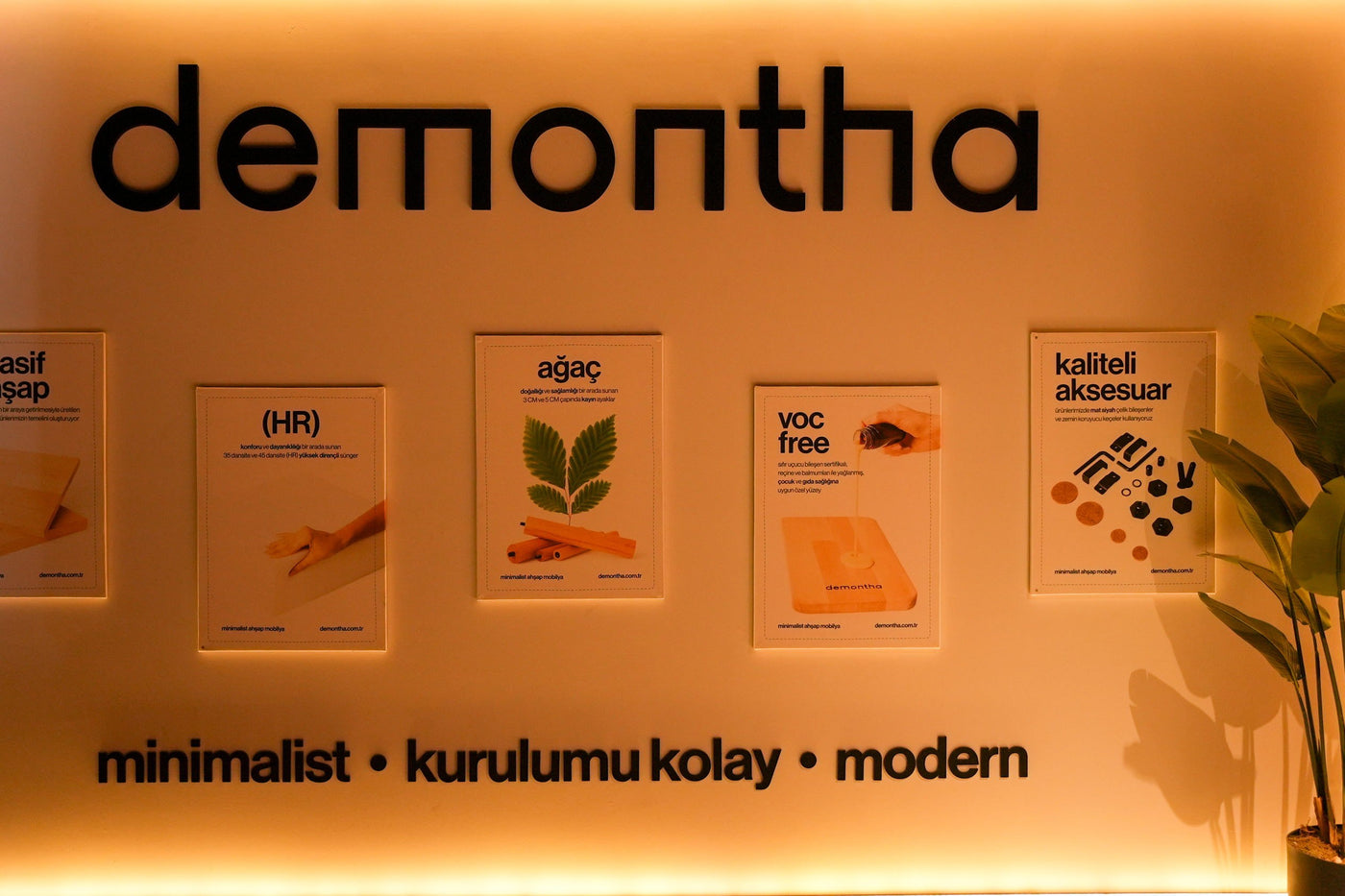 Demontha mağaza duvarında marka logosu, beş malzeme panosu ve “minimalist · kurulumu kolay · modern” sloganı