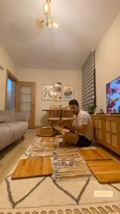 Salonun ortasında ambalajından çıkarılmış ahşap mobilya parçalarını kuran kişi